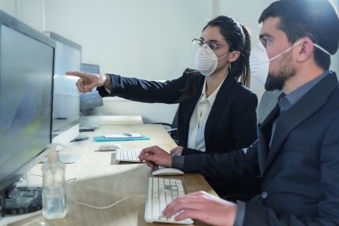 Personen mit Maske vor Bildschirmen