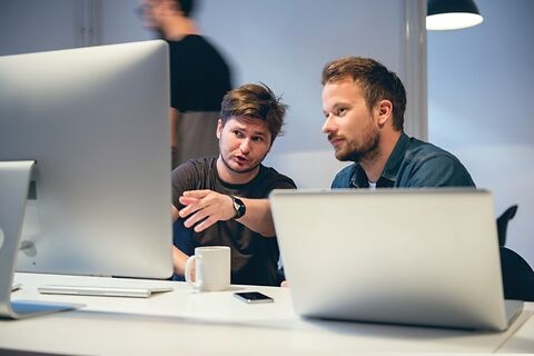 Ein Mann erklärt seinem Kollegen etwas am Computerbildschirm